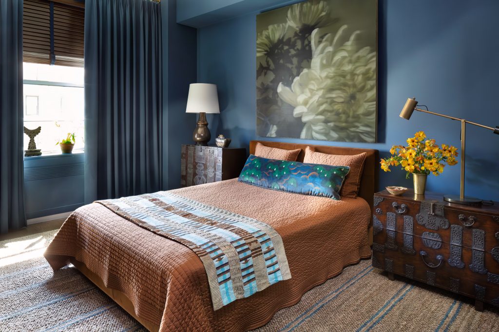 A pair of Korean blanket chests, one taller than the other, serve as bedside tables in the master bedroom. The walls are sheathed in muted sapphire and are complemented by the terracotta-toned pic-stitched bed cover. A seagrass area rug and a canvas by Southeast Asian artist Eric Chan anchor the room.